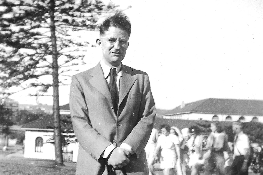 A black and white photo of a man wearing a suit standing in front of a group of women. 