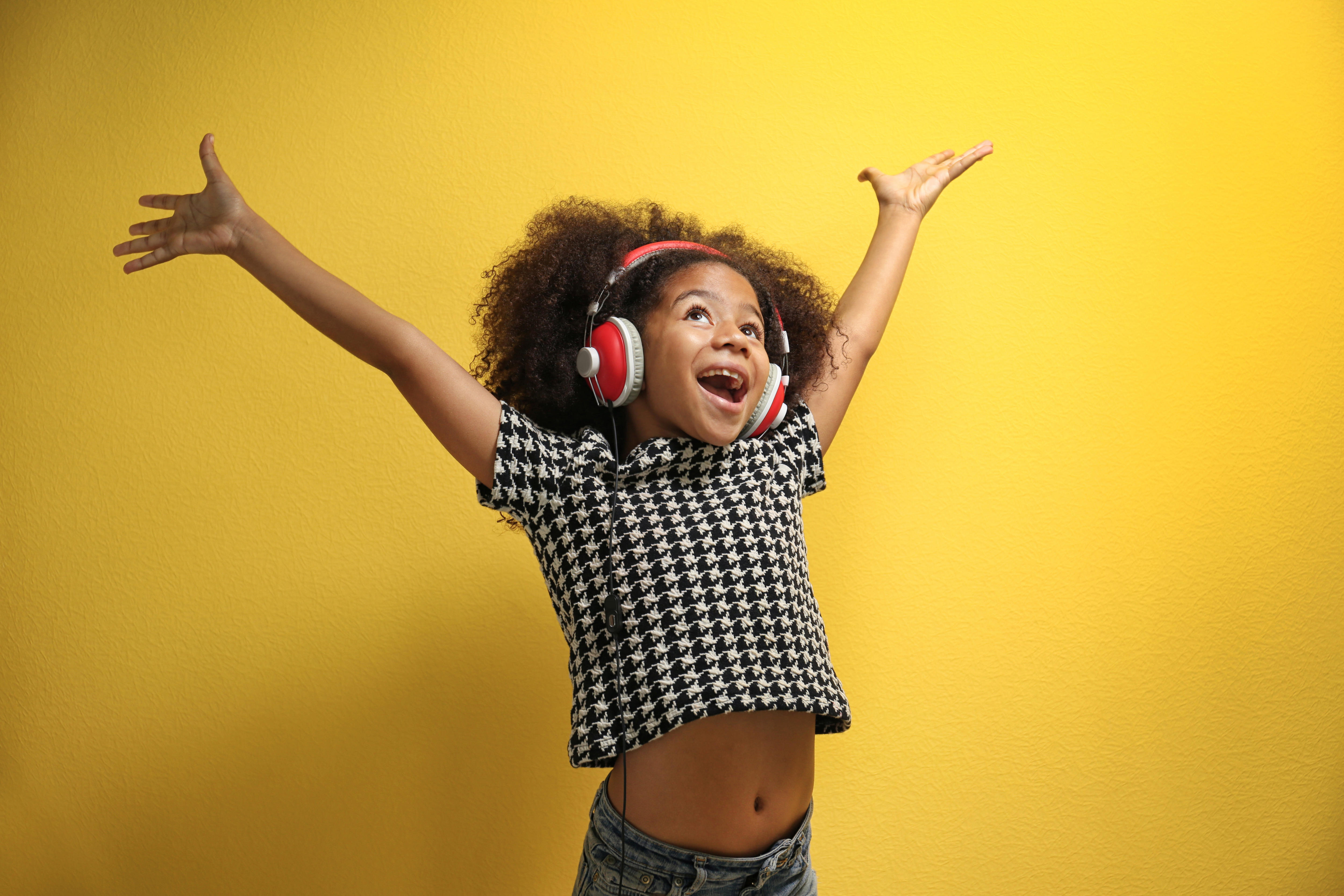 Young girl wearing headphones smiling with her arms in the air. 