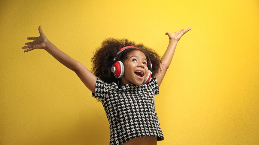 Young girl wearing headphones smiling with her arms in the air. 