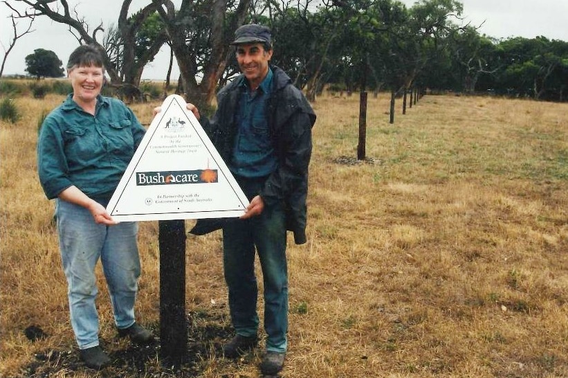 A smiling couple stand next to a sign that says Bushcare