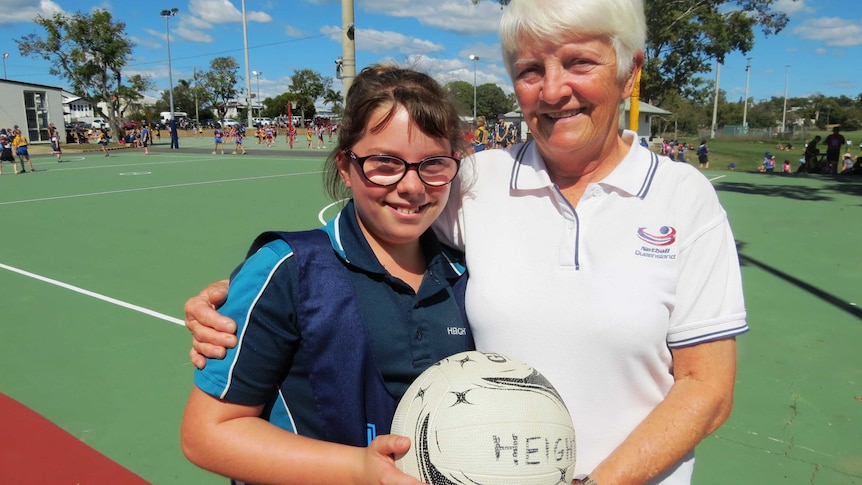 Helen Christensen and granddaughter Zoe Brown sgtand on a netball court holding a ball between them