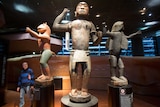 a man looks up at three wood statues in a museum