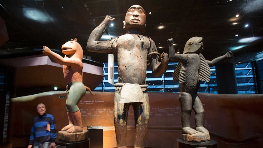 a man looks up at three wood statues in a museum