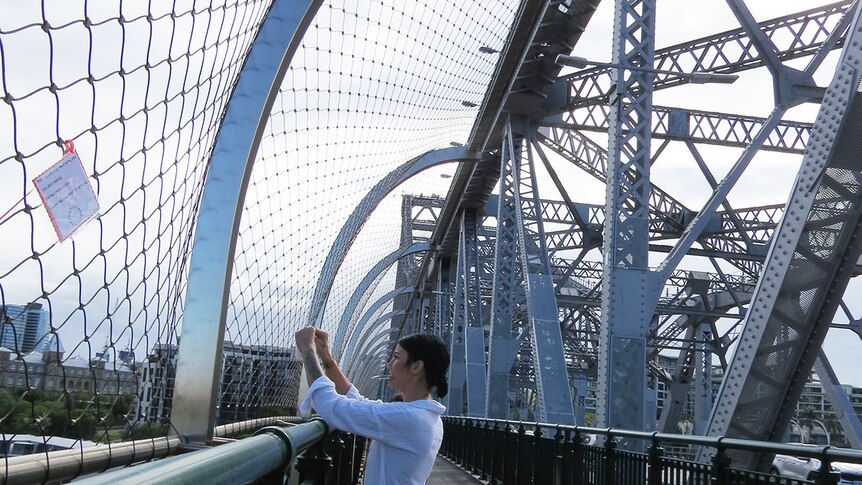 Natasha Young, founder of the Living Project, ties a support note under the suicide barrier on a bridge.