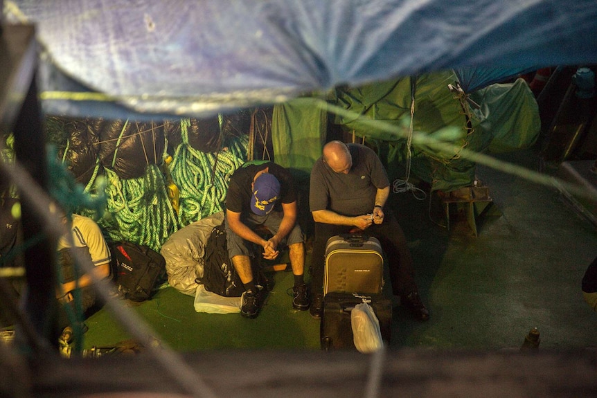 Two men sit with their heads bowed on a fishing vessel, looking defeated.