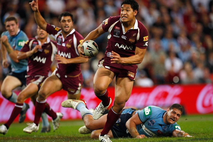 Israel Folau runs with the ball while grimacing.