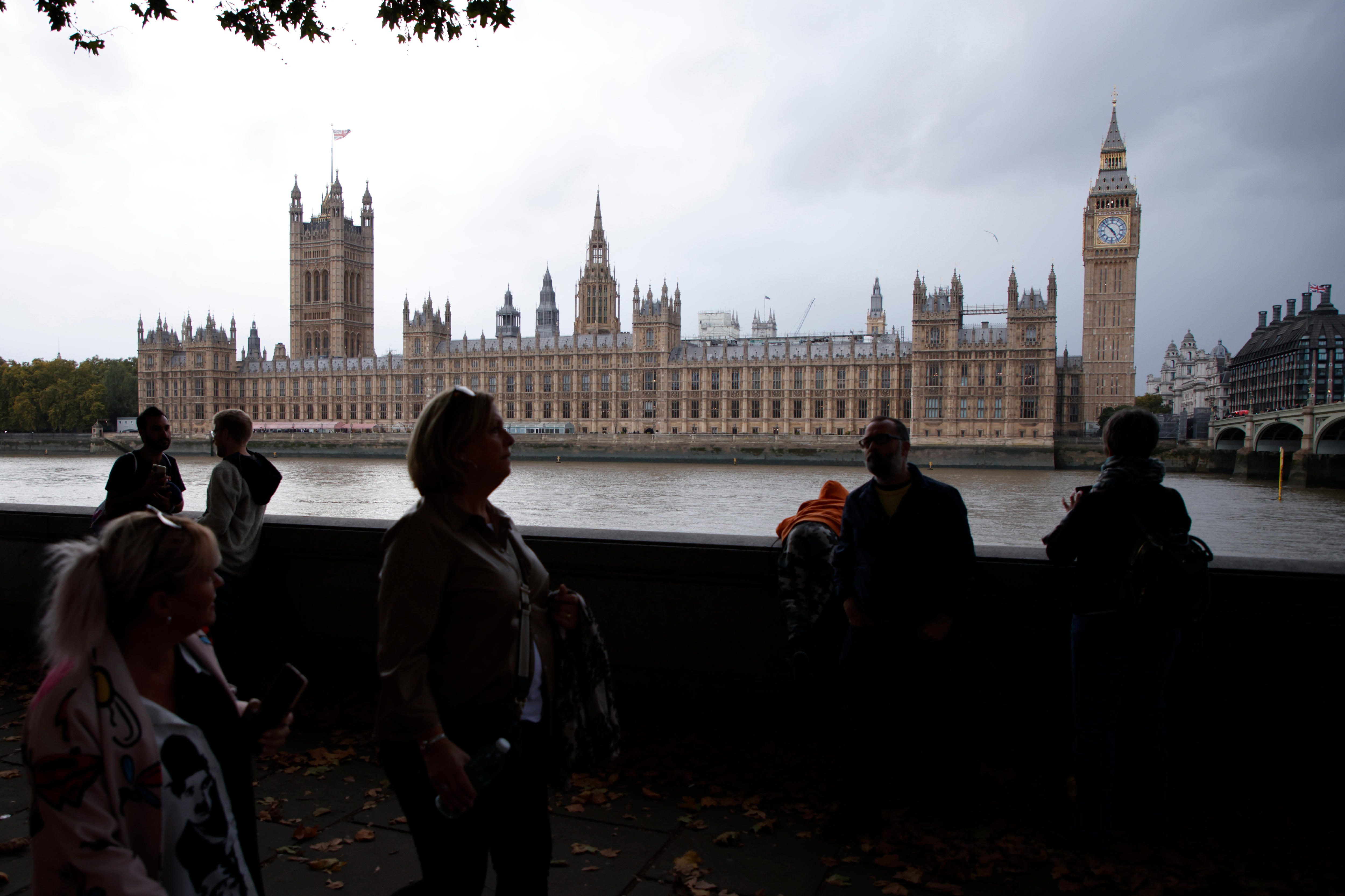 People walk past the houses of parliament in London on a cloudy day.
