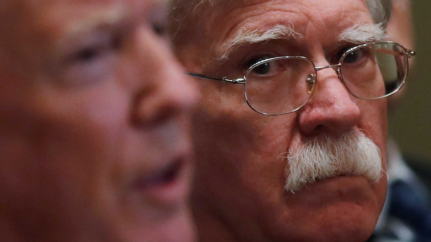 US President Donald Trump in the foreground with National Security Adviser John Bolton looking on wearing glasses