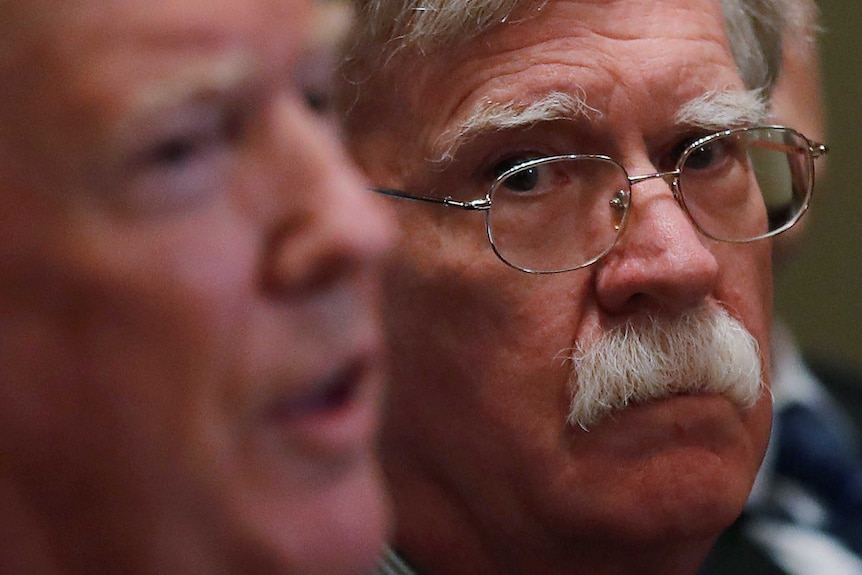 US President Donald Trump in the foreground with National Security Adviser John Bolton looking on wearing glasses