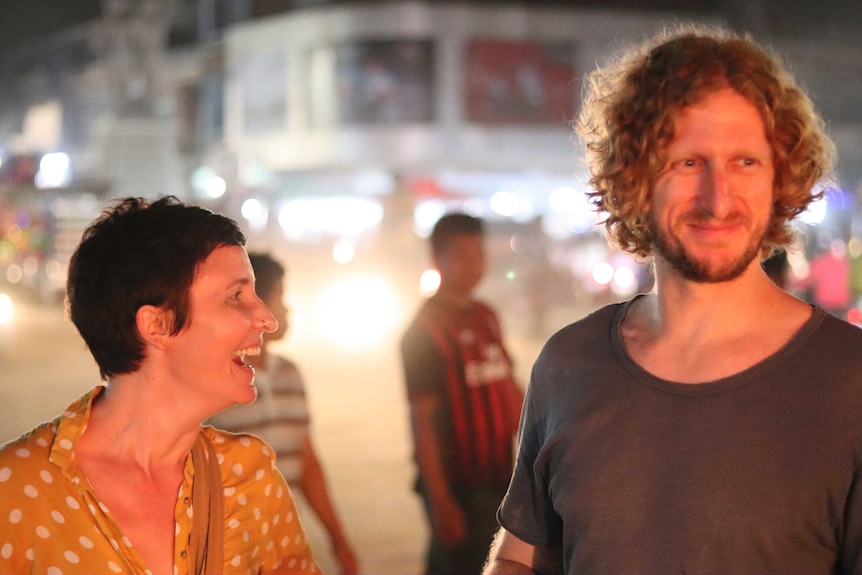 A couple smiles while standing on the streets of Cambodia at night