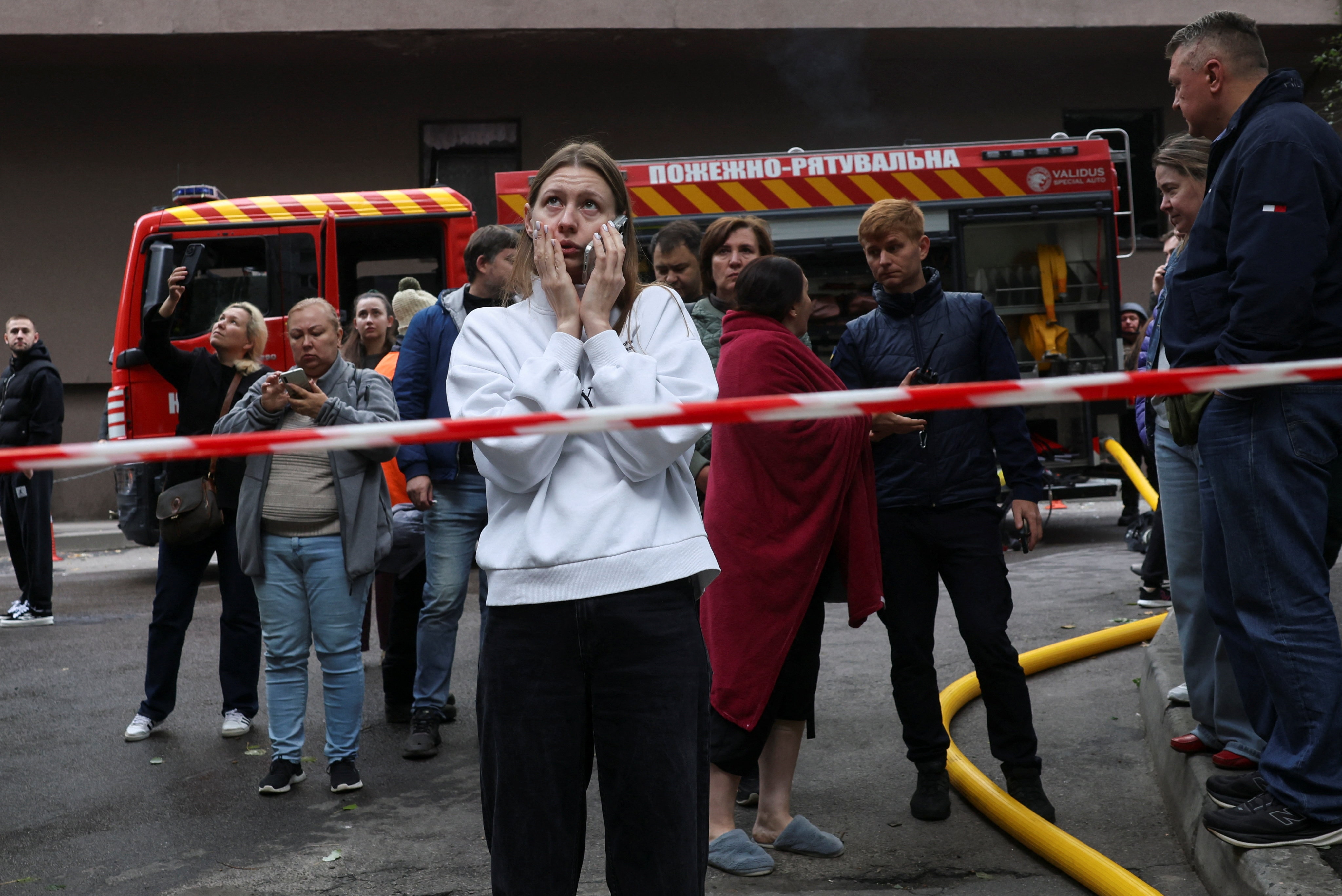 a fire truck, tape and a woman reacting to a drone strike on an apartment building