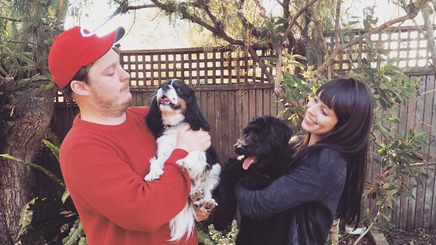 A couple in a backyard with two dogs in their arms.