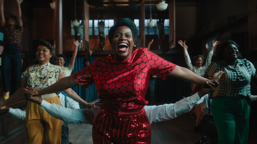 Fantasia as Celie with arms stretched out and a wide smile, dancing with glee, surrounded by others