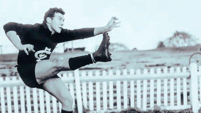 A man in a Carlton jersey in a kicking pose in a field.