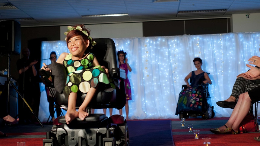 Van Theresa smiles in her wheelchair, as she moves down the audience-lined catwalk