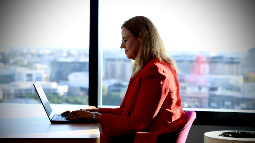 Side view of a woman seated at a desk typing on a laptop.