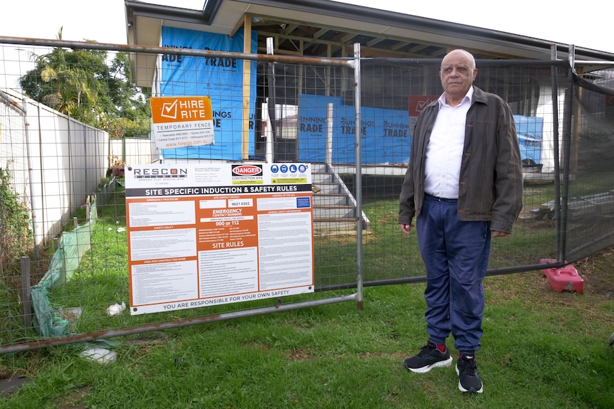 Wide shot of man standing outside a small cottage under construction