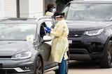 health workers in ppe stand between cars