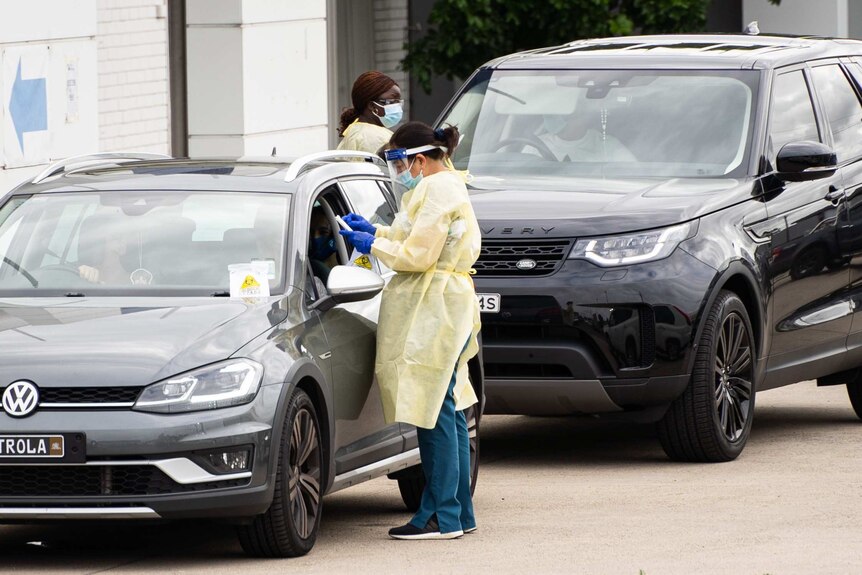 health workers in ppe stand between cars