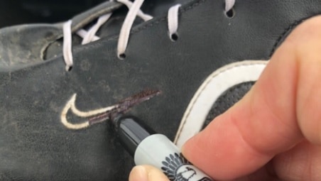 A pen is used to colour in a white Nike logo on a black shoe