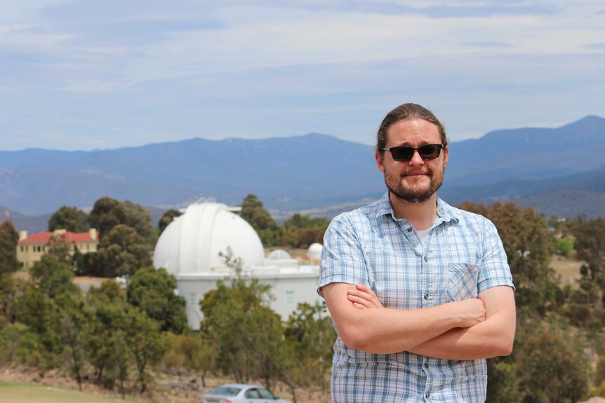 Dr Brad Tucker stands with his arms crossed at the Mt Stromlo Observatory near Canberra