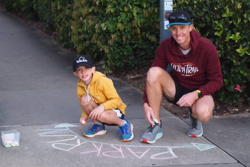 Calvin and Chris Murphy write 'parkrun' in chalk on a pavement.