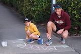 Calvin and Chris Murphy write 'parkrun' in chalk on a pavement.