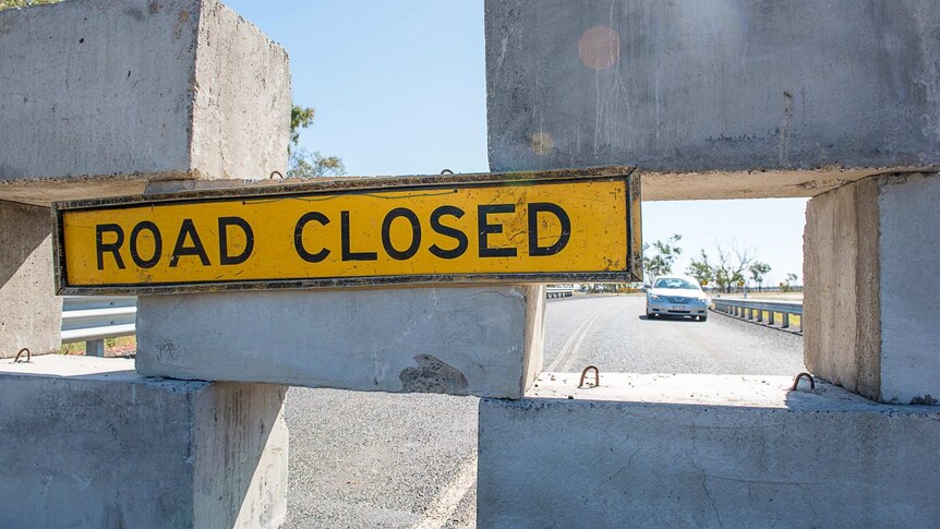 A road closed sign is hung from concrete blocks across a road bridge.