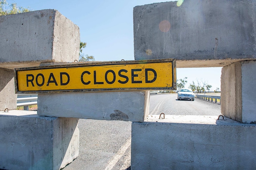 A road closed sign is hung from concrete blocks across a road bridge.