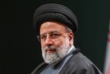 A close up of Ebrahim Raisi wearing a black turban and looking over his shoulder while wearing glasses.