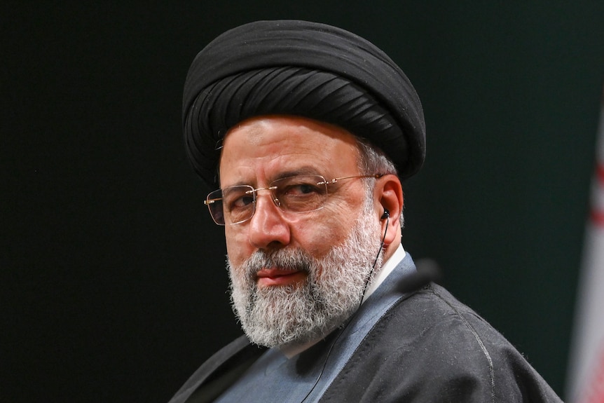 A close up of Ebrahim Raisi wearing a black turban and looking over his shoulder while wearing glasses.