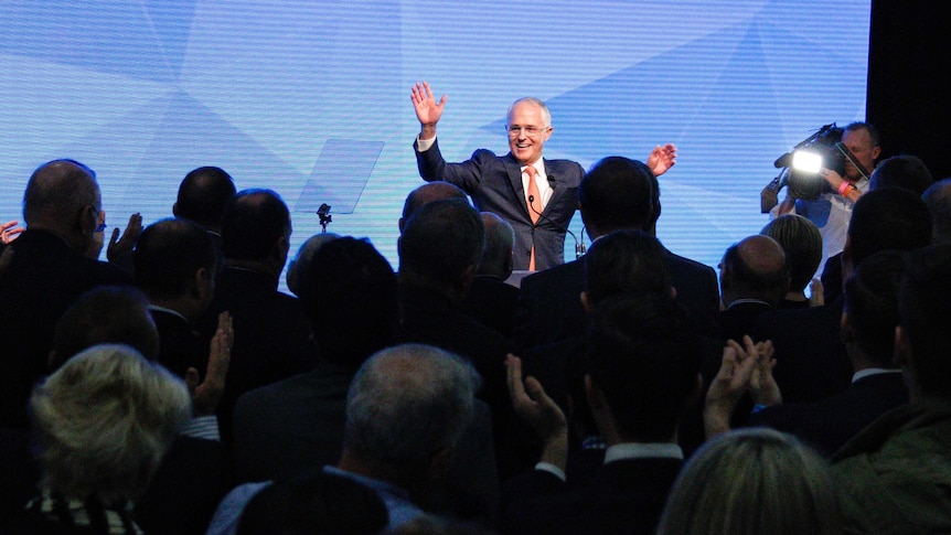 Malcolm raises his hands and smiles in front of a crowd.