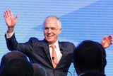 Malcolm raises his hands and smiles in front of a crowd.