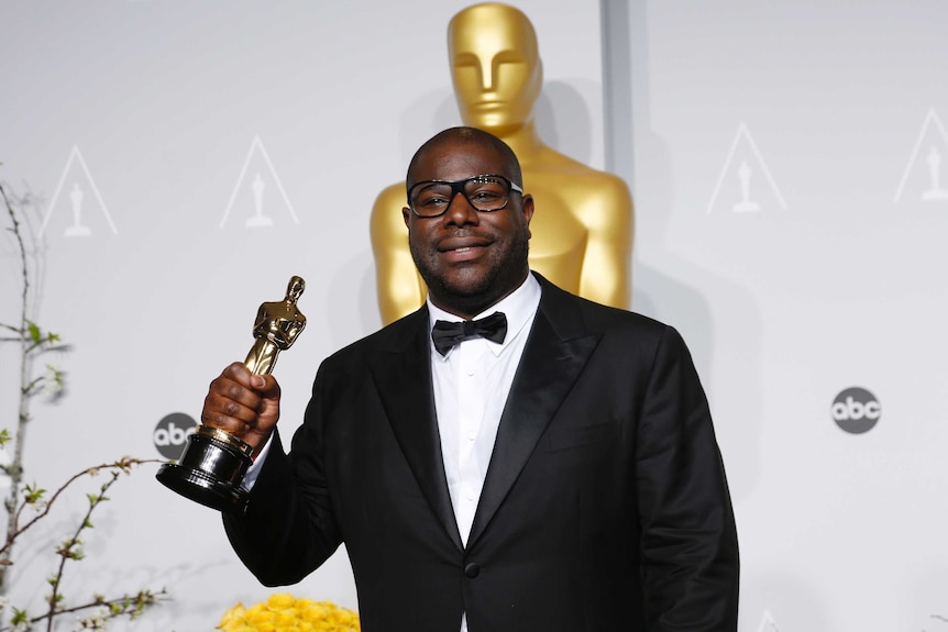 Steve McQueen, wearing a tuxedo and holding an Academy Awards for best picture.