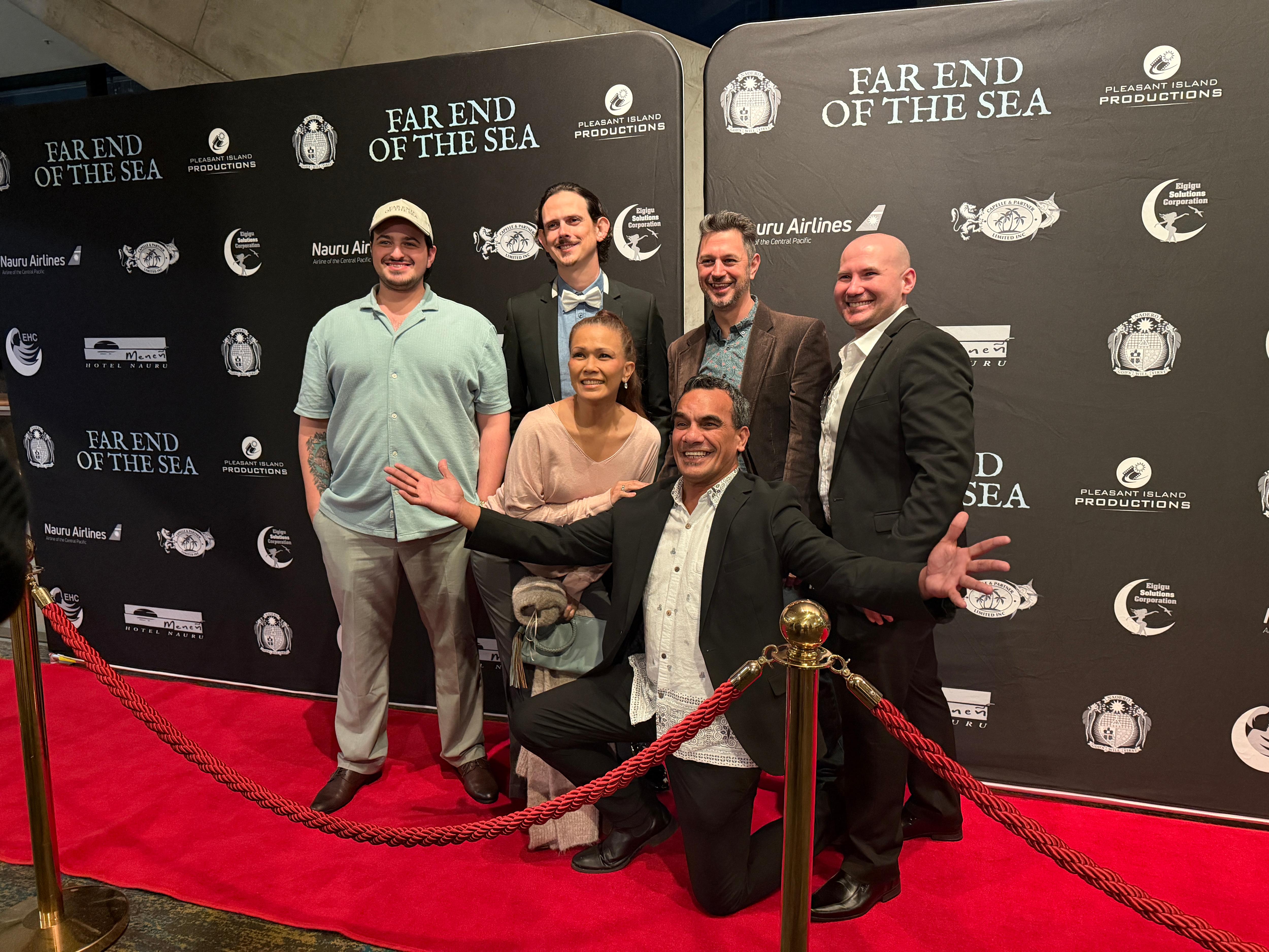 A group of people stand on the red carpet of a movie, smiling.