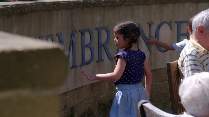 Young girl stands in front of wall with lettering 'Remembrance'