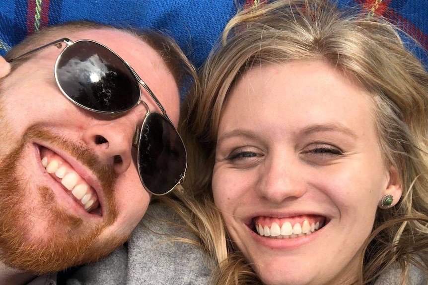 A selfie of Arron and Morgan lying outside on a picnic rug.
