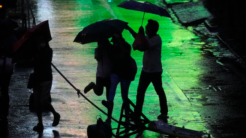 Silhouettes hold umbrellas as they walk in the rain. 