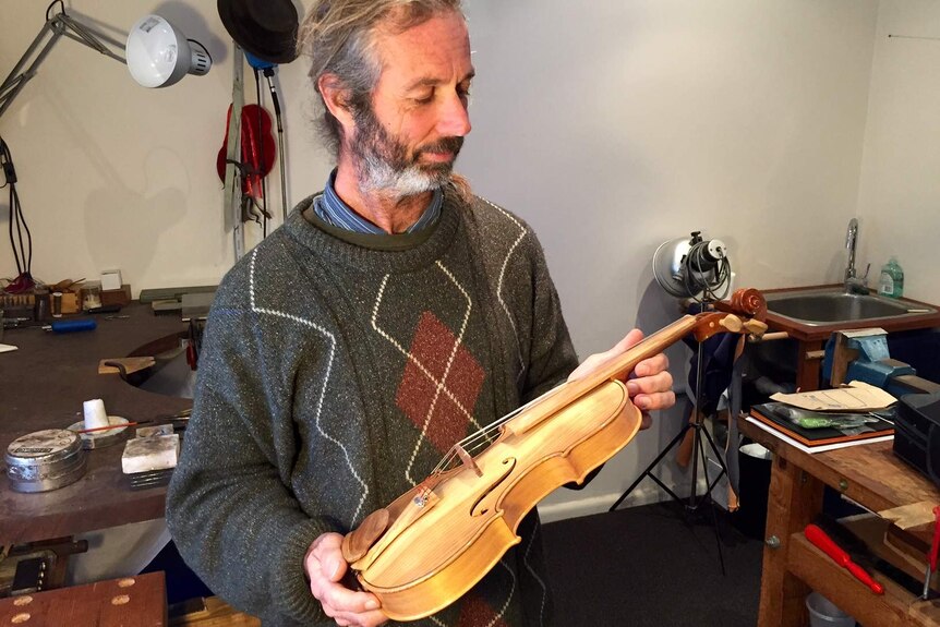 Artist Mikey Floyd holding a handmade violin in his workshop.