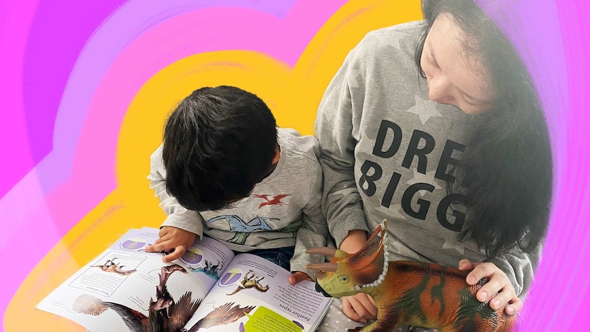 A toddler sits beside his mum looking at a book about dinosaurs in a story about parenting when English is your second language.