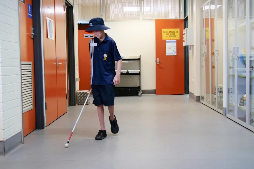 Christopher with his white cane walks down a school hallway