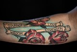 A arm tattoo with roses and bones that reads "courage, love, wisdom, strength".