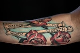 A arm tattoo with roses and bones that reads "courage, love, wisdom, strength".