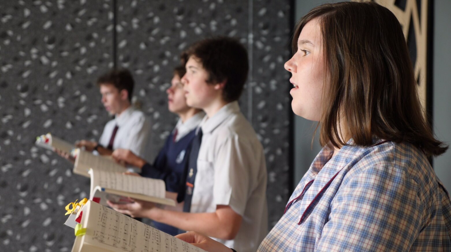 A high school girls stands in uniform singing in a choir.
