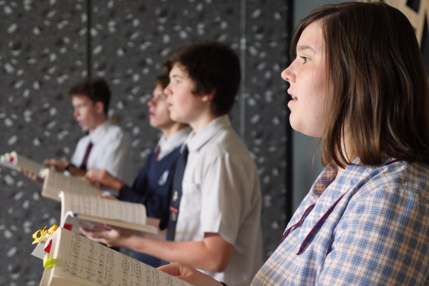 A high school girls stands in uniform singing in a choir.