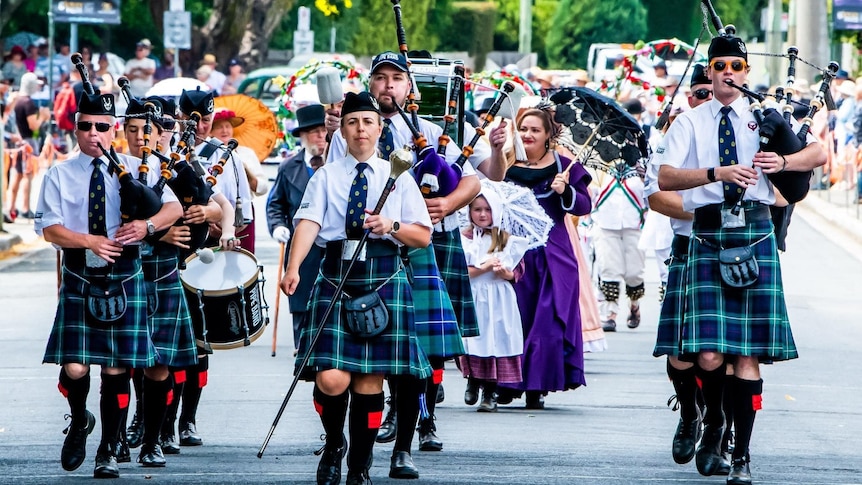 Woman leads bagpipe band down a street during a parade