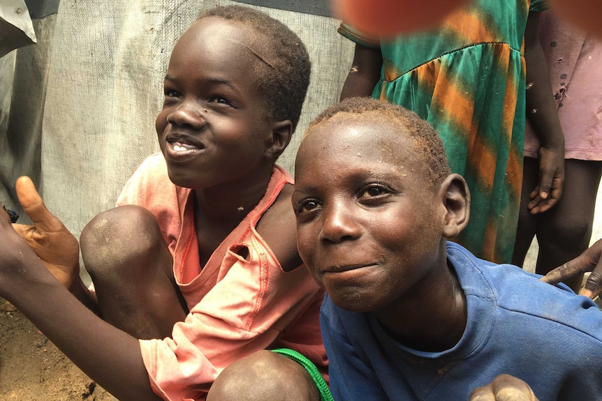 Two South Sudanese boys sitting on the ground smile as they pose for a photo.