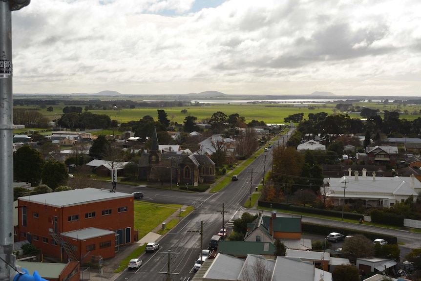 A view of a country town and the farmland, lakes and mountains beyond, taken from a high vantage point.