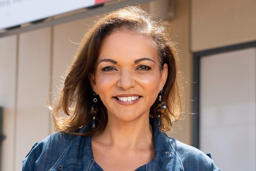 A middle aged woman with brown hair and an olive complexion smiles while standing outside her office.