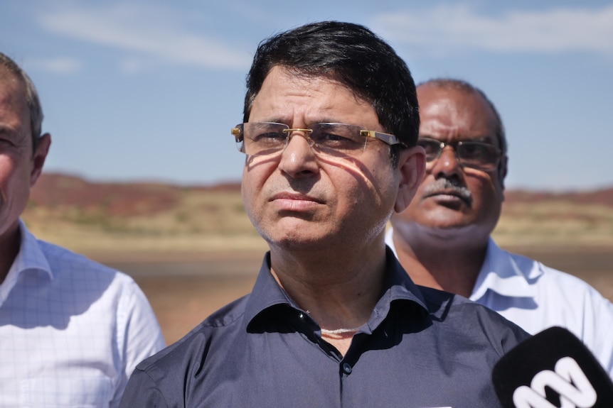 A man in a navy shirt with glasses and dark hair.